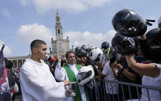 Priest flings holy water and crowd of bikers holding their helmets up.